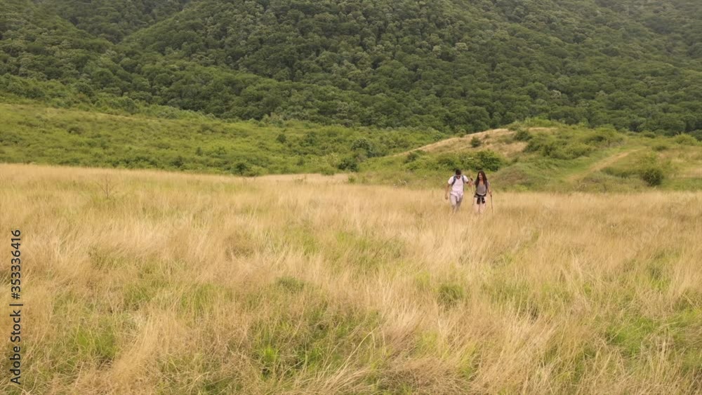 Smiling young couple walking with backpacks over green hills Smiling young couple walking with backpacks over green hills