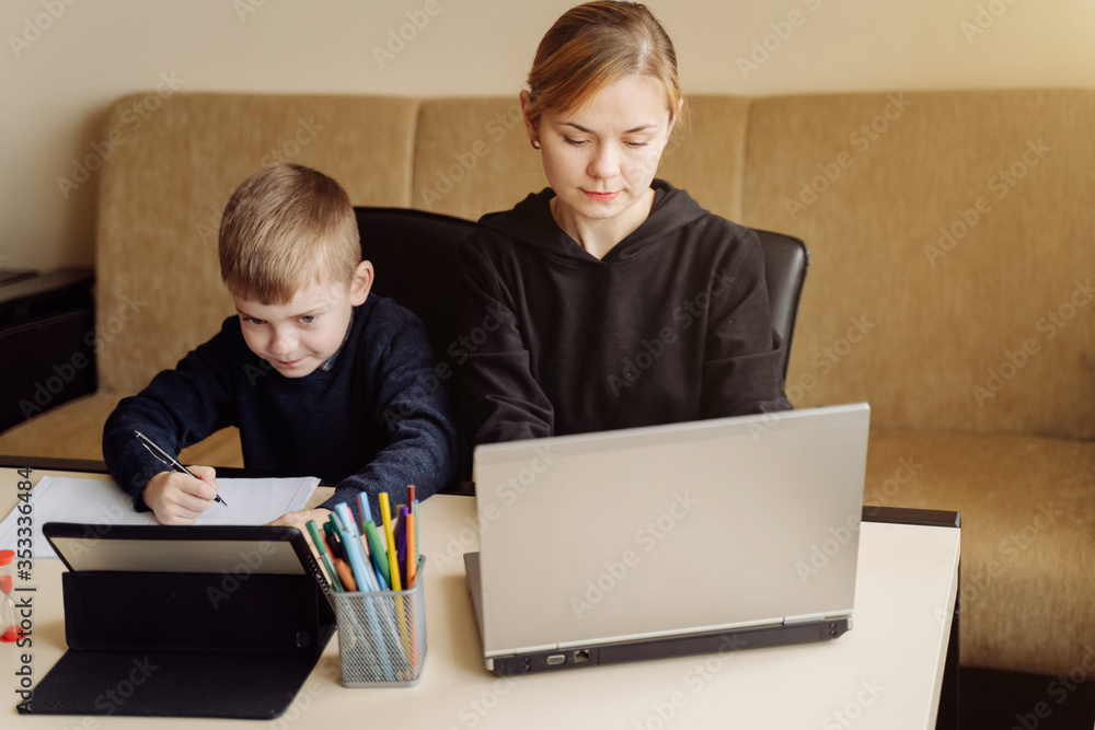 Mother using laptop and tablet teaching with her son online at home in his room Mother using laptop and tablet teaching with her son online at home in his room