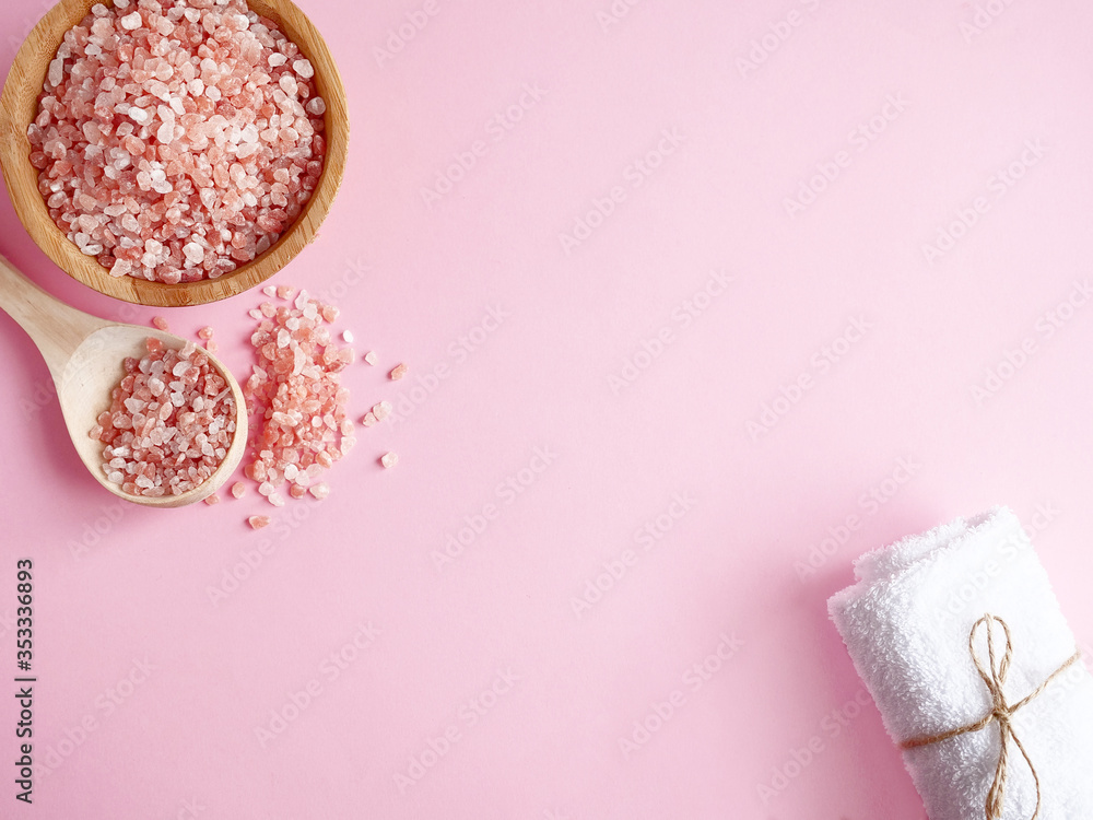 Spa flatlay composition. Sea salt in wooden jar and scattered from spoon, bath towel on pink background. Copyspace, top view. Home care concept, relax and rest, bath procedure