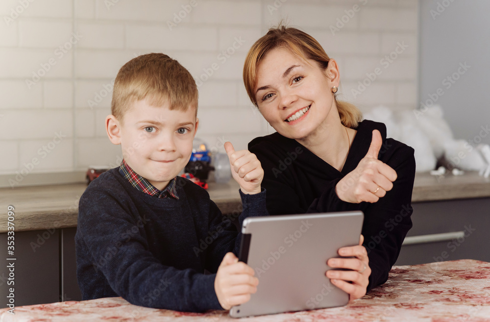 Mother using laptop and tablet teaching with her son online at home in his room Mother using laptop and tablet teaching with her son online at home in his room