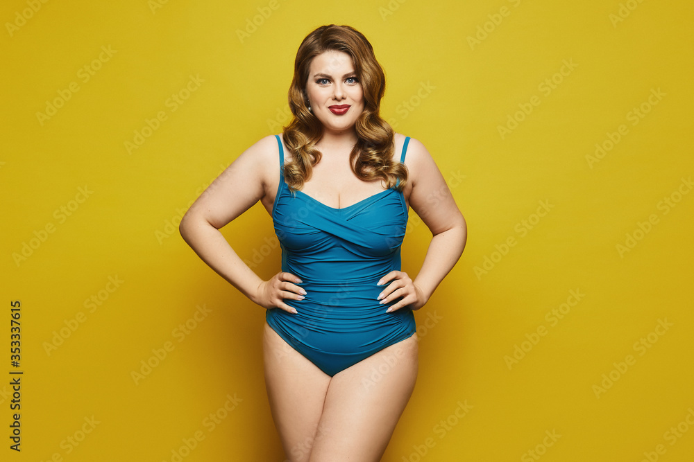 Plus-size model girl with stylish hairstyle and red lips in fashionable swimsuit at the yellow background, isolated. Fat woman in swimsuit on yellow background. Plus-size model girl with stylish hairstyle and red lips in fashionable swimsuit at the yellow background, isolated. Fat woman in swimsuit on yellow background.