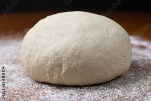 A kneaded dough with flour and water for homemade bread lying on a brown table with a black background.