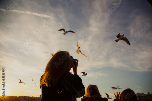 Silhouette of a girl taking a photo of a seagull from the boat on the board of a ferry at suset in Istanbul Bosphorus with blue sky and city view in the background. Travelling concept. 