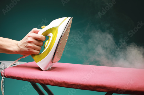 male hand holds the  modern electric iron from which steam is coming on ironing board isolated on green background photo