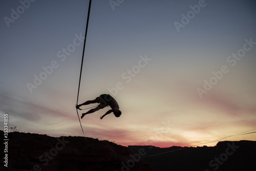 silhouette of man losing his balance on a trapeze/high-line at sunset in the mountains.