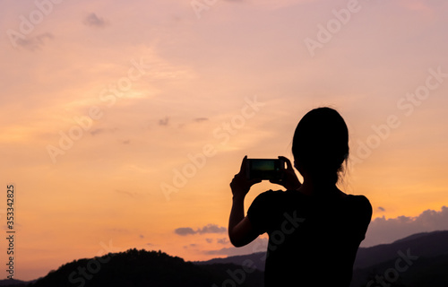 Silhouette of women taking photos of sunset with mobile phone in twilight time. Modern lifestyle