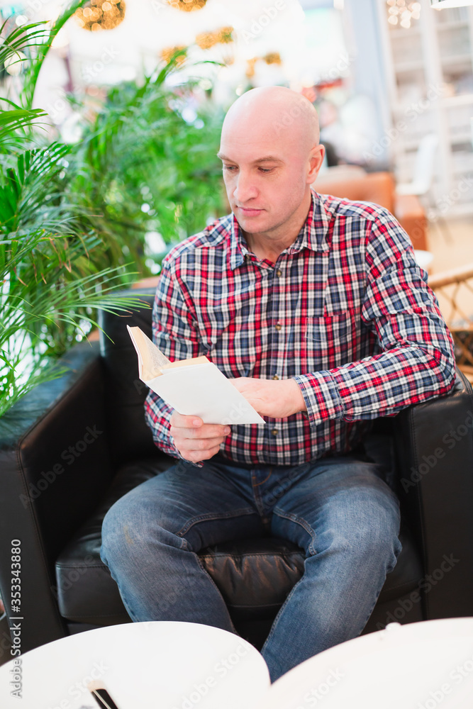 a man in a shirt sits in a chair in an apartment reading a book