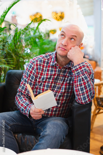 man in sitting in a chair in a bright apartment pensive with a book in his hands