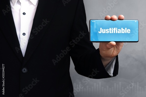 Justifiable. Businessman holding a phone in his hand. Man present screen with word. Blue Background. Business, Finance, Statistics, Analysis, Economy photo