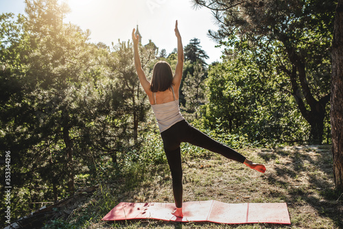 Woman doing pilates exercises in a park with trees and grass. Open air sport activities and healthy lifestyle concept. 