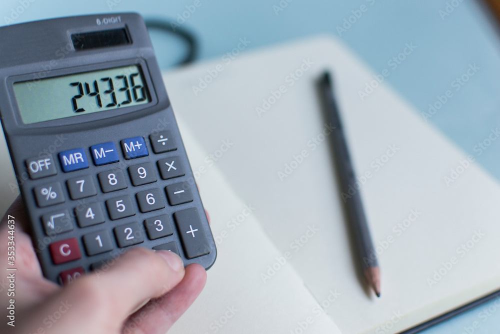 The calculator in a hand. Small accountant calculator on the background of a notebook. Calculations, records, business analytics. The calculator in a hand. Small accountant calculator on the background of a notebook. Calculations, records, business analytics.