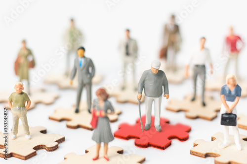 Miniature figures, Infected old person COVID-19 or coronavirus standing on red puzzles and other people standing on puzzles demonstrating the concept of social distancing to protect COVID-19 concept