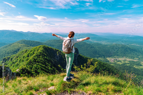 Girl tourist with a backpack stands on the edge of a cliff with outstretched arms. Hiking, tourism, freedom concept