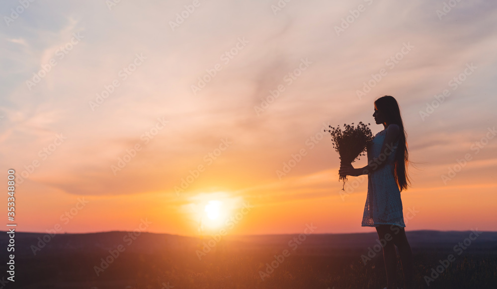 Fototapeta premium Young woman with flowers during sunset