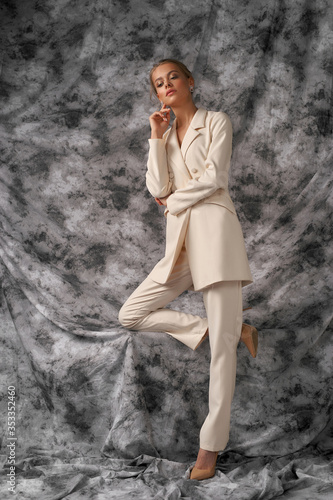 Full length fashion studio portrait. Elegant female model with makeup and hairstyle. Young caucasian woman wearing white costume. Male style clothes photo