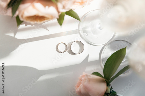 Wedding rings lie next to two glasses of champagne and a bouquet of roses in the sun