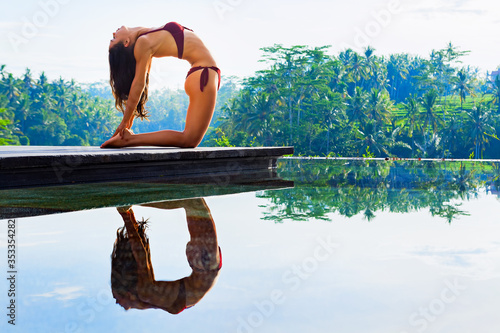 Stretching on sunrise background. Active woman in bikini practicing yoga at villa poolside to keep fit and health. Stand in ustrasana camel pose. Woman fitness, sport activity on summer family holiday photo