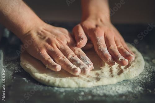 The cook uses his bare hands to roll out fresh wheat dough on a dark baking sheet to make a pizza. Home cooking.