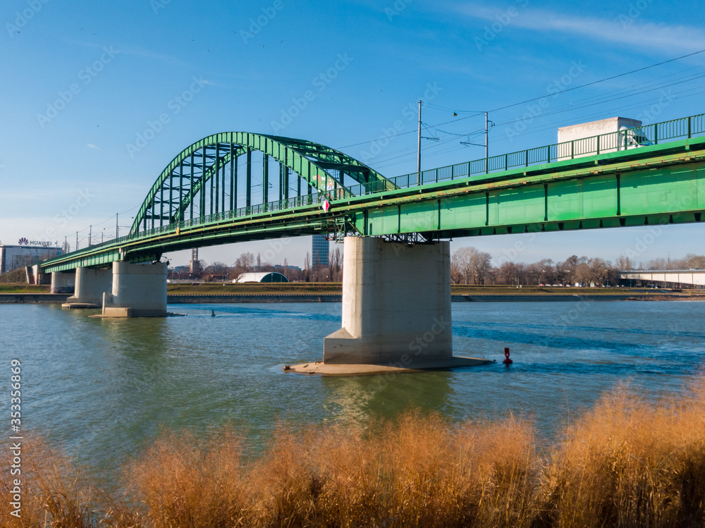 Naklejka premium Old rail Sava bridge, connecting two Belgrade shores divided by river Sava. Bright sunny day with some clouds on the horizon.