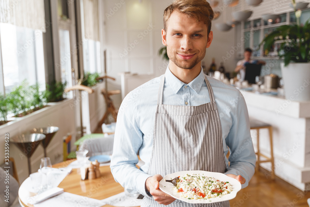 Joyful male waiter holding plate of fresh salad Joyful male waiter holding plate of fresh salad