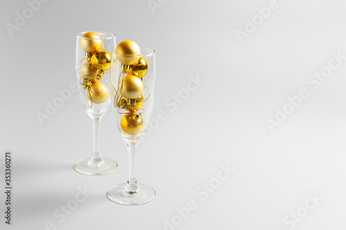 champagne glasses with golden christmas balls on gray background. New Year or Christmas party concept. copy space, minimalism