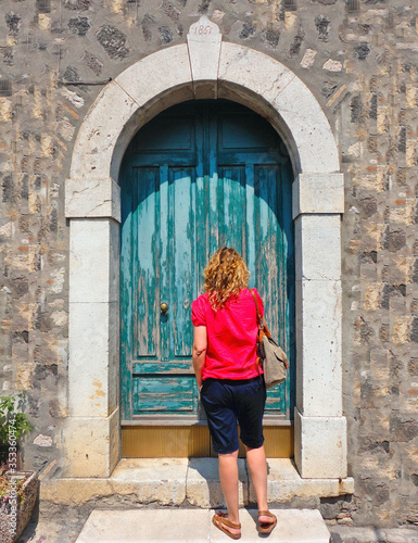 Melfi Italy. Young blonde woman with red dress knock on old wooden door of stone facade  on street of Matera, Basilicata, South Italy   © poludziber