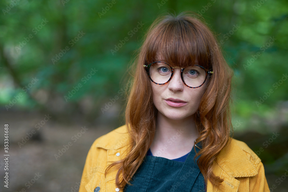 Hero shot of a Redhead girl with glasses and a yellow jacket outdoors