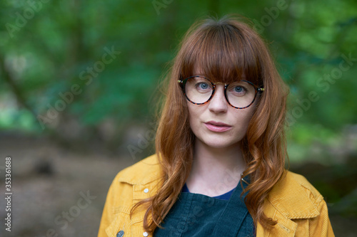 Hero shot of a Redhead girl with glasses and a yellow jacket outdoors