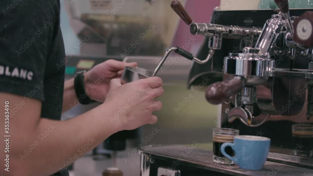 Barista steams milk in slow motion. Cafe, or coffee shop in background. Espresso shots have already been made and sit on counter to make a latte. Barista steams milk in slow motion. Cafe, or coffee shop in background. Espresso shots have already been made and sit on counter to make a latte.