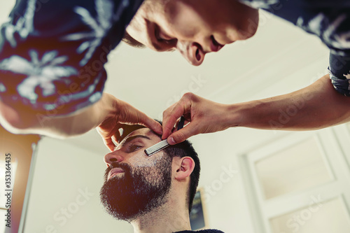 Barber shaves client's cheek with a blade