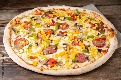 Tasty Italian pizza Mexicano on wooden background. Top view of hot pizza with chili pepper , hot sausages, onion, tomatoes and cheese. Flat lay. Advertising photo for a site or menu.