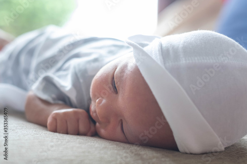 The portrait of cute little baby infant boy wearing white hat lay to sleep prone on the bed,