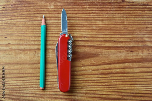 multi-tool swiss army red knife and geen pencil isolated on wooden background