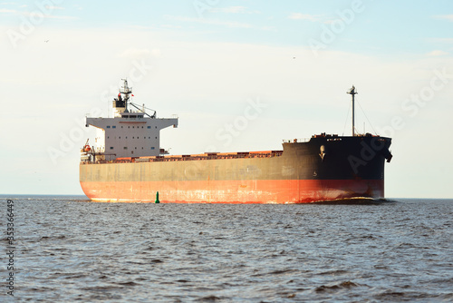 Large bulk carrier (cargo ship) sailing in an open sea from Europoort. Clear blue sky with cirrus clouds. Rotterdam, Netherlands. Global communications, logistics, industry theme photo