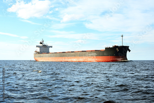 Large bulk carrier (cargo ship) sailing in an open sea from Europoort. Clear blue sky with cirrus clouds. Rotterdam, Netherlands. Global communications, logistics, industry theme photo