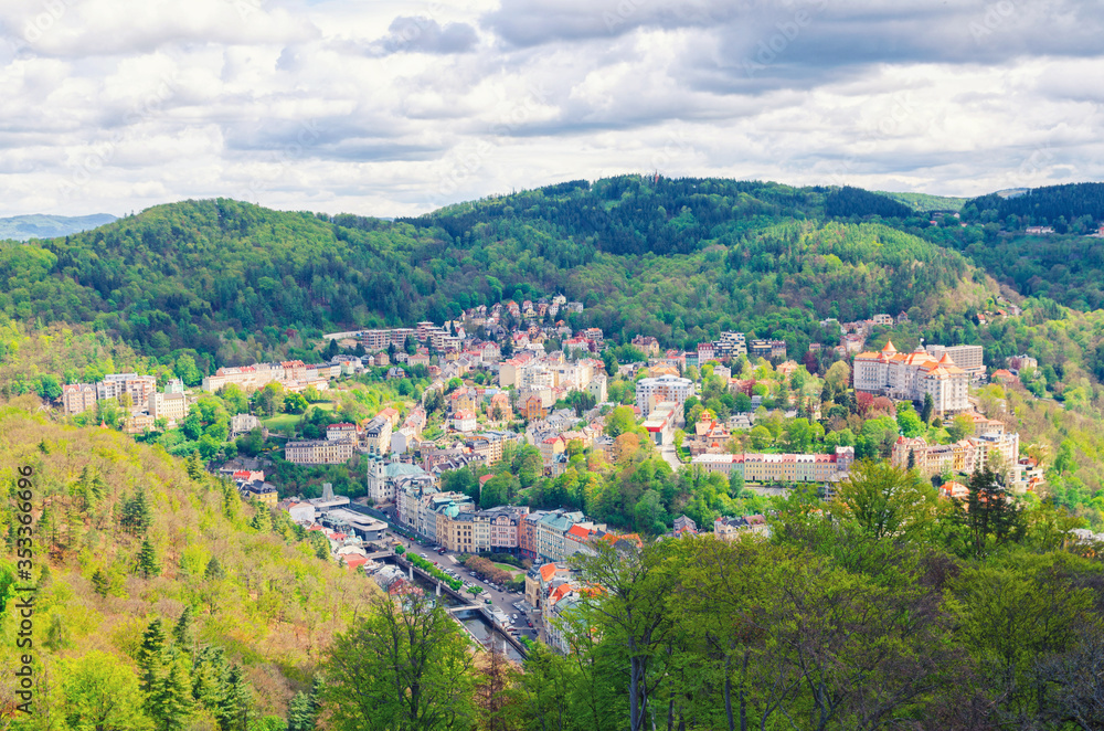 Top aerial panoramic view of Karlovy Vary (Carlsbad) spa town with colorful beautiful buildings, Tepla river and hills of Slavkov Forest with green trees, West Bohemia, Czech Republic