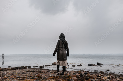 Young Women in rainjacket standing at coastline in rainy weather and clouds