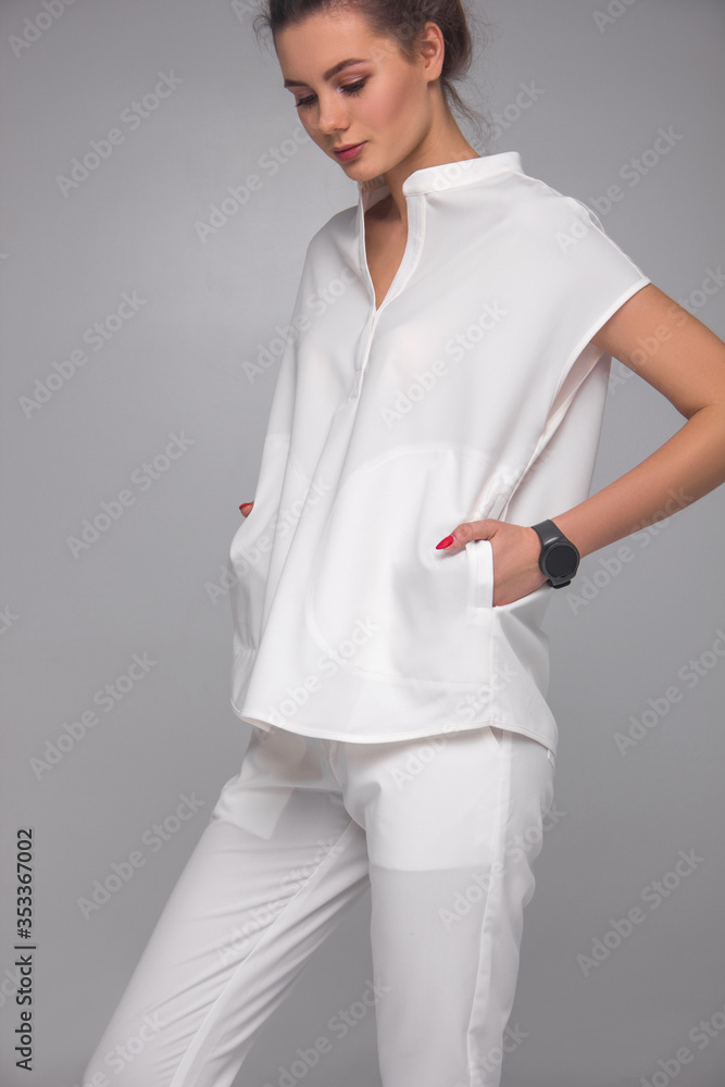 close-up of stylish nurse's white medical costume. young doctor teacher is standing with hands in her pockets on gray wall background. medical fashion concept. free space close-up of stylish nurse's white medical costume. young doctor teacher is standing with hands in her pockets on gray wall background. medical fashion concept. free space
