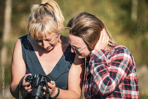Two women looking at photos on a digital lens reflex camera in summer © mrpluck