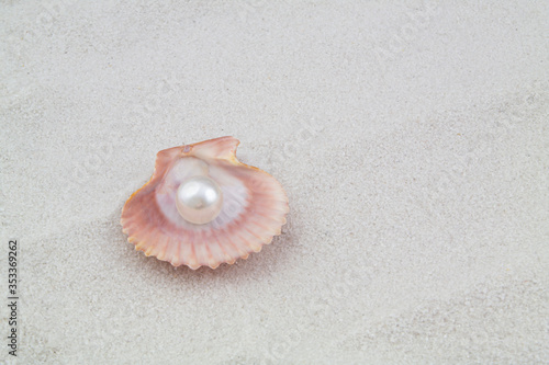 Pearl in seashell on white sand background with copy space