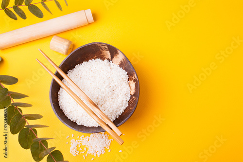 Coconut bowl with Chinese rice and Chinese chopsticks on a yellow background. Organic food