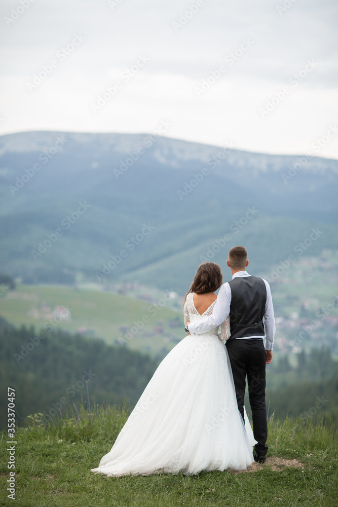 Wedding. The bride and groom running through the mountain slope. After wedding session. The guy in the white shirt and waistcoat, and a girl in white dress walk on the green glade in the mountains