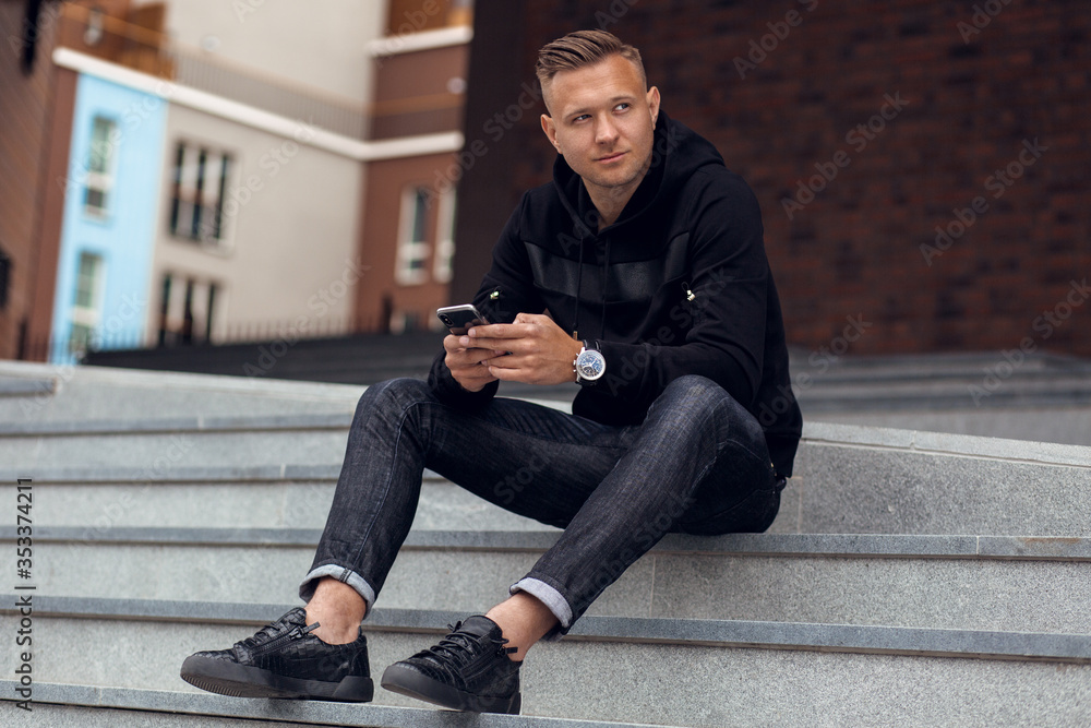 Blond male model posing in casual black clothes outdoor