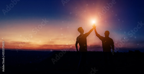 Two silhouette man colliding hand, showing success on the top of the hill in twilight, concept teamwork.