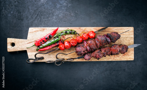 Traditional Russian shashlik on a barbecue skewer with vegetable and sumach as top view on a wooden cutting board with copy space