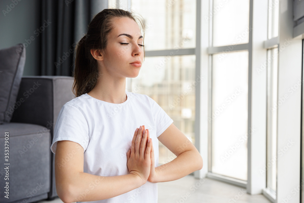Image of woman holding palms together while sitting on yoga mat