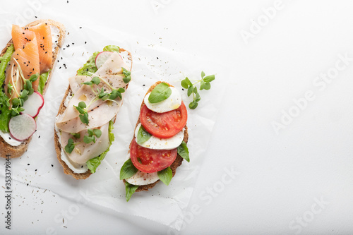 sandwiches with ham, radish, romano salad, baby basil, mascarpone cheese, caprese salad on a white background. copy space. top view.