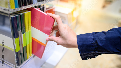 Male hand customer choosing new red paper notebook from display rack in stationery shop. Buying office supply concept