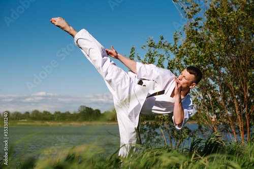 A man karate fighter in white kimono training outdoor in the park