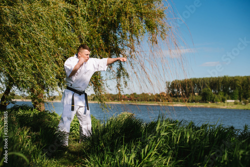 A man karate fighter in white kimono training outdoor in the park